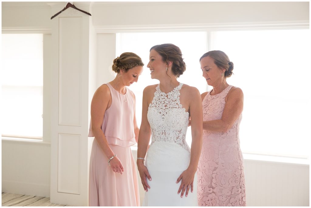 The mother of the bride and the Maid of Honor help Jamie get into her wedding dress. 